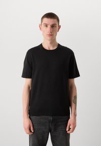 Zwarte katoenen T-shirt met korte mouwen en geribbelde ronde hals. Bevat een klein embleem op de borst en heeft een rechte zoom. Draag het met een donkere spijkerbroek.