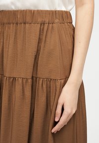 Κοντινό πλάνο στο χέρι ενός ατόμου που ακουμπά δίπλα σε καφέ, ψηλόμεση, πιετωμένη φούστα με υφασμάτινη υφή.