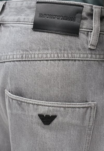 Grå denimjeans med et svart lærbeltepatch preget med "EMPORIO ARMANI" og et trekantet logo over lomma bak.