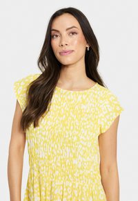 Robe jaune avec un imprimé animal blanc, à manches courtes et volantées, et une texture froncée. Tissu lisse avec une coupe décontractée.