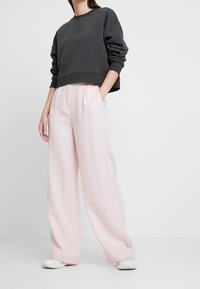 Oversized black sweatshirt with crew neck, paired with light pink linen wide-leg pants. White sneakers complete the look.