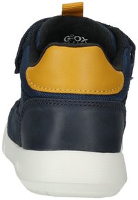 Scarpa blu navy con un accento giallo sul tallone, presenta una tomaia strutturata e una suola in gomma bianca. Include una chiusura con cinturino regolabile.