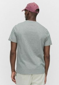 Grå kortärmad t-shirt med en mjuk textur, med rundad halsringning. Tillsammans med en ljus färgad keps i en dämpad rosa nyans.