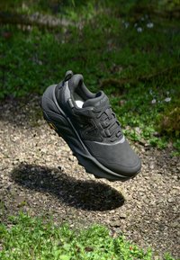 Încălțăminte de drumeție neagră, cu o parte superioară texturată, sistem de închidere cu șireturi și talpă din cauciuc proeminentă. Talpa exterioară Vibram vizibilă și amortizare pentru suport.