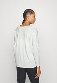 Light gray long-sleeve shirt, soft fabric, relaxed fit, wide neckline, and subtle seam details, paired with dark leggings.