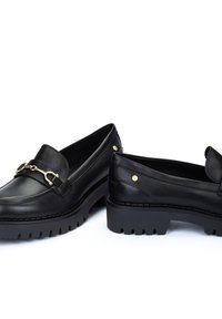 Mocasines de cuero negro con un acento de hardware en tono dorado, suela texturizada y puntas redondeadas; con sutiles remaches dorados en el tacón.
