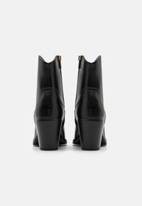 Botas de tobillo de cuero negro con un tacón afilado, que cuentan con un cierre de cremallera en la parte trasera y una textura suave.