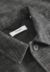 Halli halli mustriga jakk, millel on must sisepind, nuppude sulgemine ja silt, millel on kirjas "GABBA."