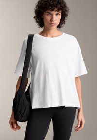 Vit t-shirt med kort ärm gjord av bomull, med en lös passform och rundad halsringning, ihop med svarta leggings och en puffig svart väska.