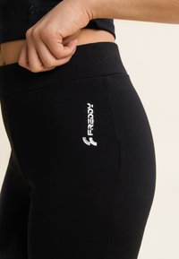 Mallas negras confeccionadas en tela elástica, con una textura suave. Destacado logo blanco impreso en el muslo izquierdo. Diseño ajustado alrededor de la cintura.