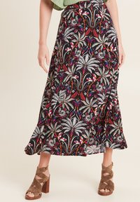 Lange, zwarte maxi-rok met kleurrijke bloem- en abstracte patronen. Heeft een uitlopende vorm en een lichte split, gecombineerd met bruine haksandalen.