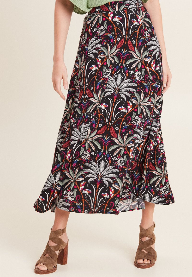 Lange, zwarte maxi-rok met kleurrijke bloem- en abstracte patronen. Heeft een uitlopende vorm en een lichte split, gecombineerd met bruine haksandalen.