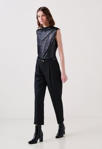 Top nero senza maniche con texture lucida, abbinato a pantaloni neri a righe sottili e stivaletti neri con tacco; design complessivo elegante.