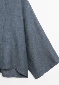 Volný dlouhý rukáv s širokým rukávem a rovný lem z modrošedé lněné látky s texturou, s viditelným švem.