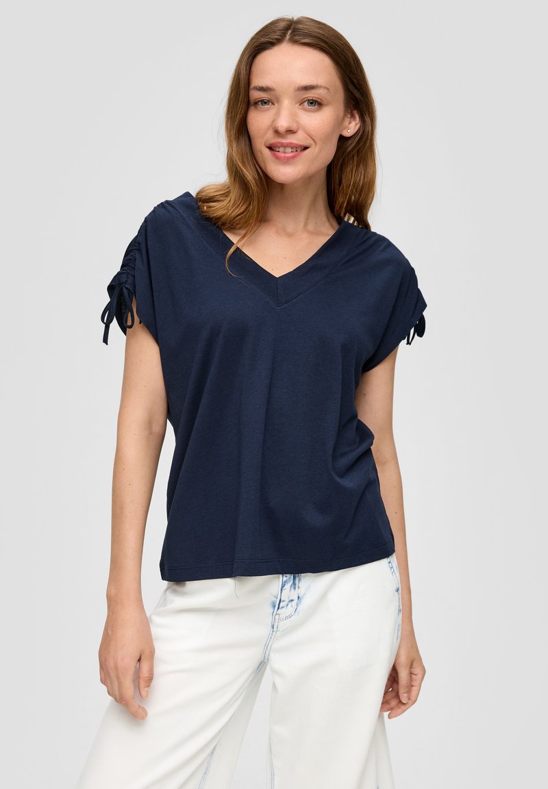 Granatowa koszulka typu V-neck z krótkimi rękawami z detalami związania. Wykonana z miękkiego materiału, luźny krój i gładka tekstura.