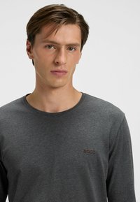 Donkergrijze long-sleeve t-shirt van zacht materiaal, met een ronde halslijn en een klein rood "BOSS" logo op de linkerborst.
