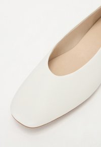 Ballerines en cuir blanc avec un bout carré arrondi, texture lisse et semelle basse et structurée, adaptées à un usage quotidien.