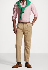 Lichtroze overhemd met knopen, groene trui om de nek gedrapeerd, beige broek, bruine instapschoenen, gemusterde sokken en een zilveren horloge.