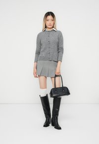 Grå strikket cardigan med fem knapper, grå plisserte miniskjørt, svarte knelange støvler og liten svart håndveske. Hvite knestrømper inkludert.