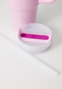 Pink reusable cup with a textured surface, clear lid, and purple rubber sealing mechanism; includes a white straw beside it.