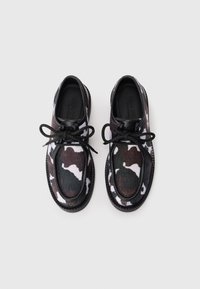 Chaussures à lacets avec motif camouflage, arborant des couleurs marron, noir et blanc, réalisées en tissu texturé et dotées d'une semelle en caoutchouc noir. Lacets noirs inclus.