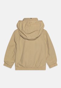 Beige huva jacka med elastiska muggar och midja, med en diskret logotyp på baksidan. Slät tyg med avslappnad passform och minimalt med detaljer.
