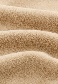 Beige, tekstureret stof med en blød, fuzzy overflade; har glatte, buede folder, der viser dybde og ensartet farve gennem hele stoffet.