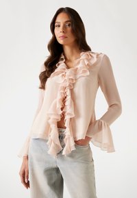 Rosa blus i blush med volangkrage och volangärmar, i ett lätt och texturerat tyg med en avslappnad passform. Matcherad med ljusblå jeans.