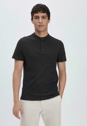 Korte mouwen zwarte henley shirt met ronde hals, driehoekige knoopsluiting en zachte katoenen stof, gecombineerd met lichtgekleurde broek.