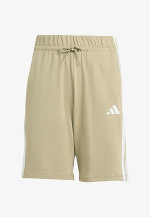 Twee kinderen staan rug aan rug, gekleed in bijpassende beige Adidas shorts en T-shirts met witte strepen, witte sokken en zwart-witte sneakers.