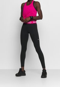 Pink Nike tanktop med sorte stropper, sorte leggings med en pink logo-linning og sorte løbesko. Glat stof og tætsiddende design.