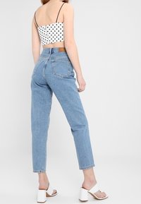 Ljusblå högmidjade jeans med rak benbena, tillsammans med en svart och vit prickig croppad topp. Vita blockklacksandaler.