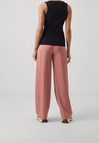 Top nero a coste senza maniche abbinato a pantaloni morbidi rosa chiaro e larghi. I pantaloni presentano un design a gamba ampia e una caduta delicata, migliorando il comfort.