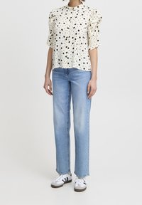 White blouse with black polka dots, puffed short sleeves, and a mandarin collar. Paired with light blue straight-leg jeans and sneakers.