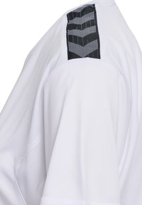 Biała koszulka z krótkim rękawem z czarnym, fakturowanym akcentem w zygzakowaty wzór na ramieniu. Gładka tkanina o luźnym kroju.