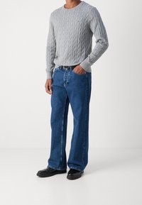 Grauer Cable-Knit-Pullover, blaue gerade geschnittene Jeans und schwarze Schuhe. Der Pullover hat ein strukturiertes Muster; die Jeans sind im verwaschenen Look.