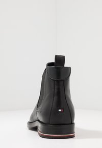 Botas de piel negras hasta el tobillo con lados elásticos, punteras redondeadas, un pequeño tacón y un parche de logo con acentos en rojo, blanco y azul.