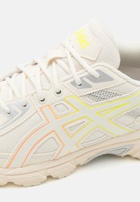 Valge võrgusilma toss, millel on heledates hallides aktsentides ja mitmevärviline "Asics" logo. Tekstuuriga ülevõtted ja pehmendustega tallakujundus.