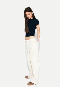 Zwarte cropped t-shirt en crèmekleurige wijdvallende cargo broek met zijzakken. Bruine instappers met een luipaardprint.