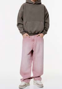 Sweat à capuche gris avec poche avant, associé à un jean oversize rose clair. Les chaussures sont des baskets couleur crème avec des accents clairs.