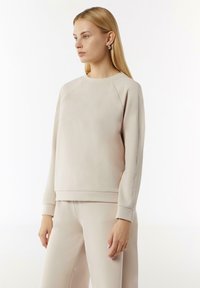 Beige sweatshirts met een ronde halslijn, raglanmouwen en geribde manchetten. Gladde textuur met contrasterende naaddetails. Gecombineerd met bijpassende broeken.