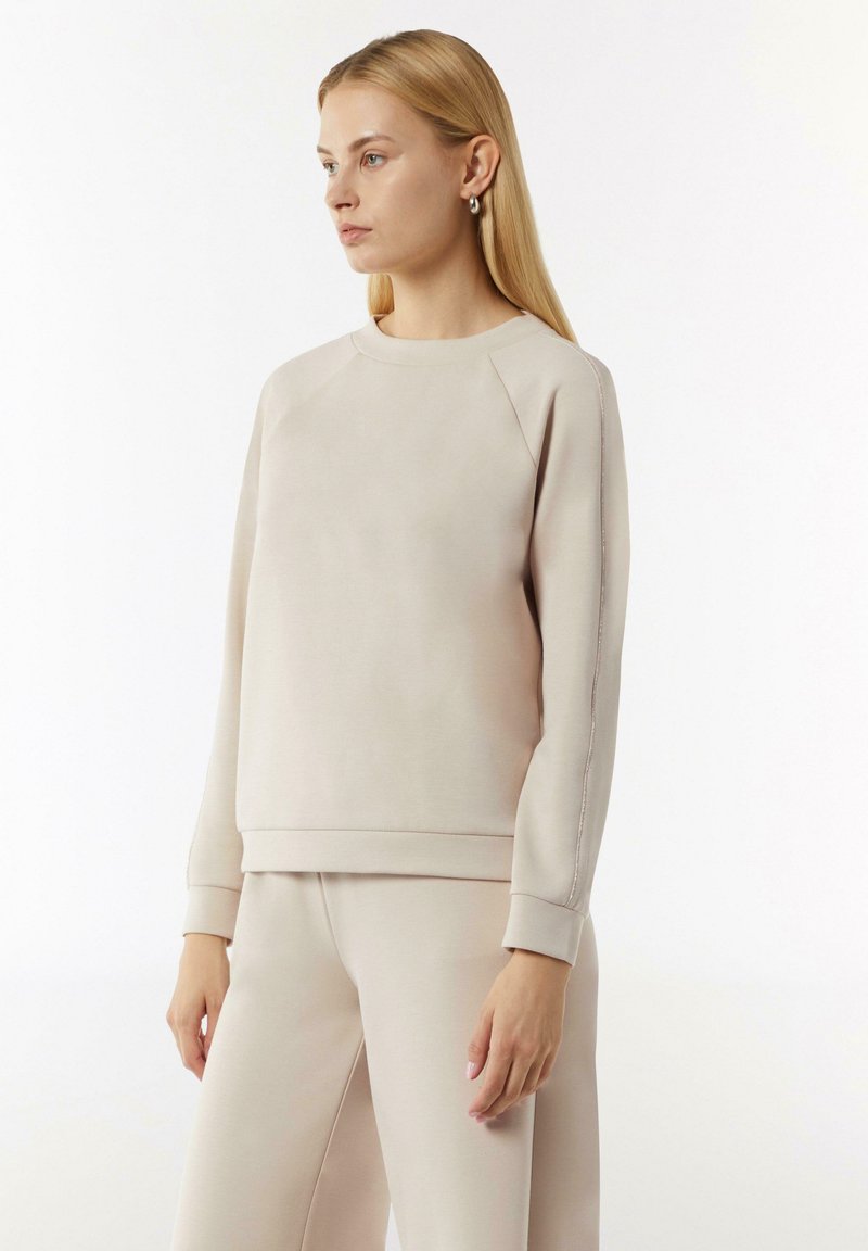 Beige sweatshirts met een ronde halslijn, raglanmouwen en geribde manchetten. Gladde textuur met contrasterende naaddetails. Gecombineerd met bijpassende broeken.