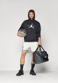 Sort hættebluse med Jordan-logo, lyse mesh-shorts med sorte striber, sort basketball og en sort Nike duffeltaske.
