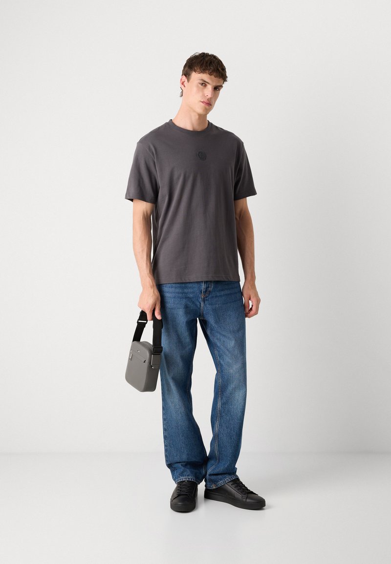 T-shirt en coton gris avec un col rond, jeans en denim bleu, baskets noires et un petit sac bandoulière gris avec une sangle.