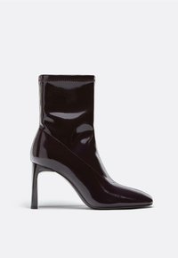 Kiiltävä, tumma violetti nilkkuri, jossa on terävä kärki ja hoikka korkea korko. Silkkinen pinta, jossa on tiukka ja istuva muotoilu sekä vähäistä ommelta.