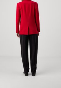 Červený přizpůsobený blejzr s dlouhými rukávy, rovného střihu a zadním rozparkem, v kombinaci s černými širokými kalhotami a černými botami.
