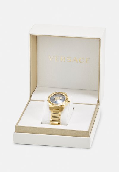 Gold Versace watch with a lion emblem on a blue dial, set in a white box with gold accents and plush interior.