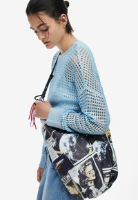 Must kott, millel on retro kosmoseteemalised graafika ja illustratsioonid. Kandmiseks õlal, värvilise nöördetailiga. Hele sinine kampsun avatud võrgumustriga.