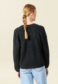 Svart stickad tröja med rund halsringning, avslappnad passform, sänkta axlar och långa ärmar, kombinerad med ljusblå jeans.