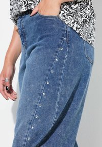 Džínové kalhoty světle modré barvy s volným střihem. Mají stříbrné cvočky podél postranního švu. Spárovány s topem v černobílém vzoru.